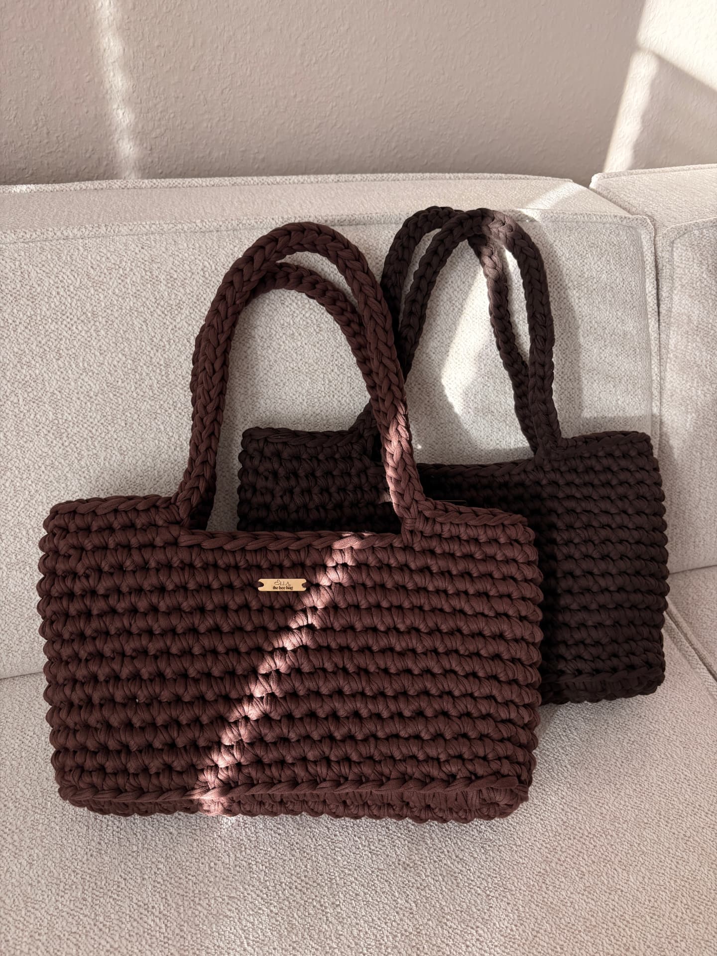 Zwei gehäkelte ELLA Taschen auf einem hellen Sofa